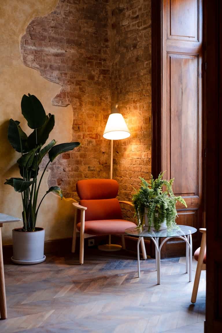 Warm living space featuring a red brick wall, armchair, glow from a lamp, and houseplants.