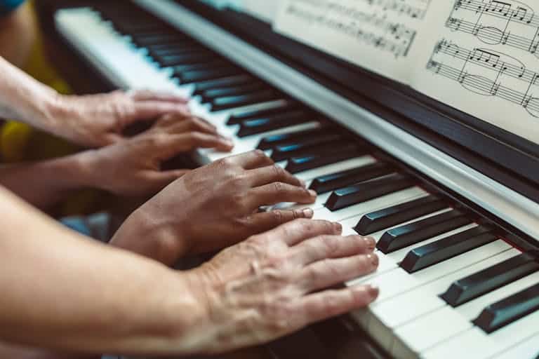 Close-up of hands playing a piano with visible sheet music, showing a teaching tutorial.