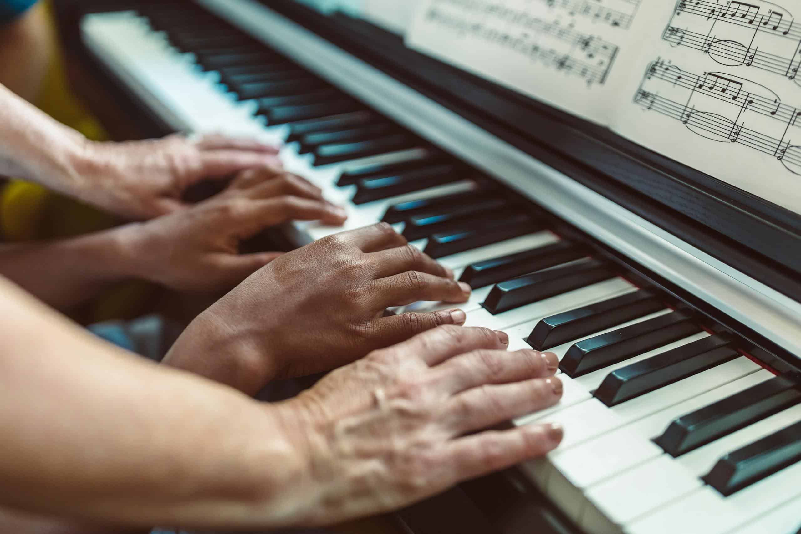 Close-up of hands playing a piano with visible sheet music, showing a teaching tutorial.