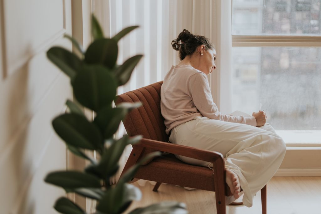 Woman relaxing on a chair by a window, deep in thought, indoors.